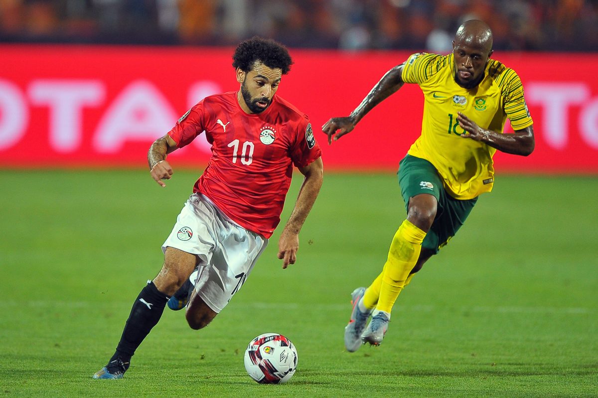 Egyptian soccer player Mo Salah runs with the ball away from South African defender.